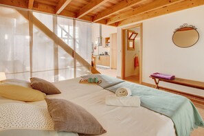 A bedroom with a bed, pillows, a bedside table, a mirror, and a view of a kitchen and bathroom through a sliding door.