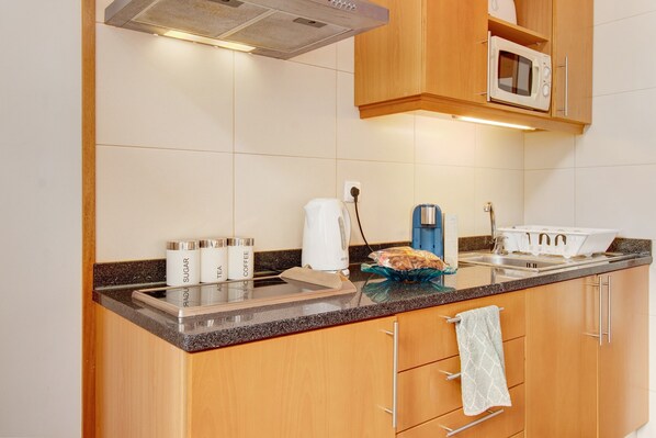 A kitchen with wooden cabinets, a microwave, a kettle, and a coffee maker.
