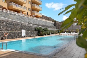 A swimming pool with a stone wall, lounge chairs, and a building with balconies.
