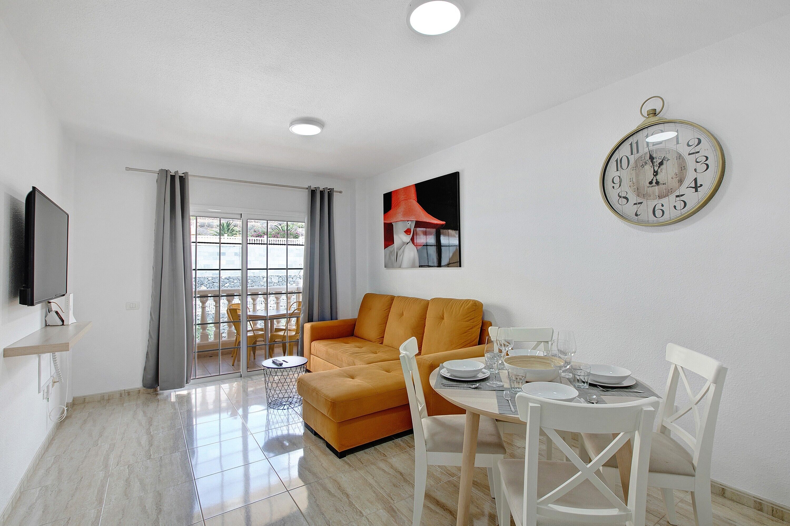 A modern living room with a sofa, dining table, chairs, a TV, and a wall clock.
