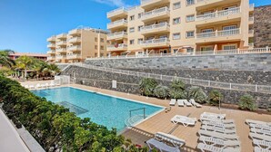 Ein Hotel mit Schwimmbad, mehreren Balkonen und einer Steinmauer.