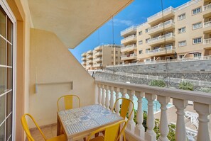 A balcony with a table and chairs, overlooking a pool and adjacent buildings. - Holiday Home Palmar D10 with Shared Pool, Balcony and Wi-Fi (Palm-Mar)