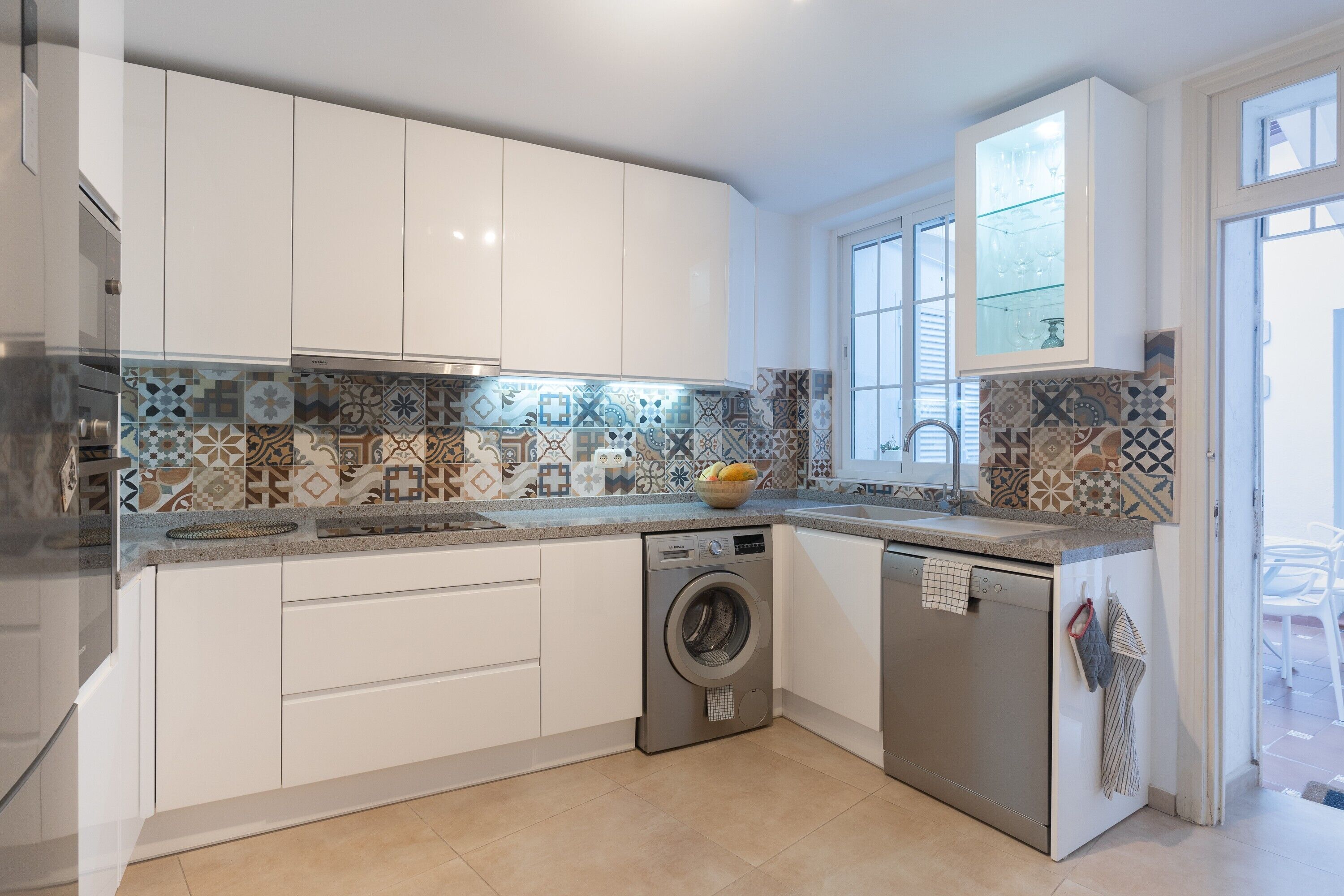 A modern kitchen with white cabinets, a washing machine, and a window.