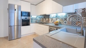 Eine moderne Küche mit weißen Schränken, Edelstahlgeräten, einer gemusterten Spritzschutzplatte und einer Arbeitsplatte aus Granit.