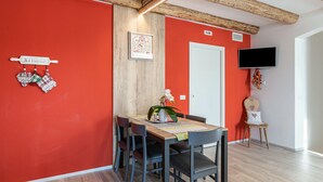 Ein Essbereich mit roter Wand, Holzbalkendecke, einem an der Wand montierten Fernseher und einem Tisch mit Stühlen.