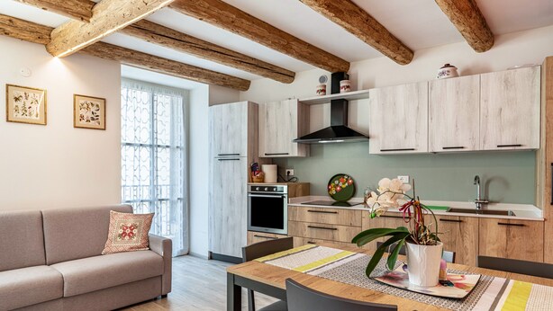 Eine moderne Küche mit Holzbalken, einem Essbereich mit Tisch und Stühlen sowie einer Couch mit dekorativen Kissen.