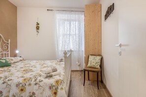 A bedroom with a bed, a chair, a window with sheer curtains, and a wooden wall panel.