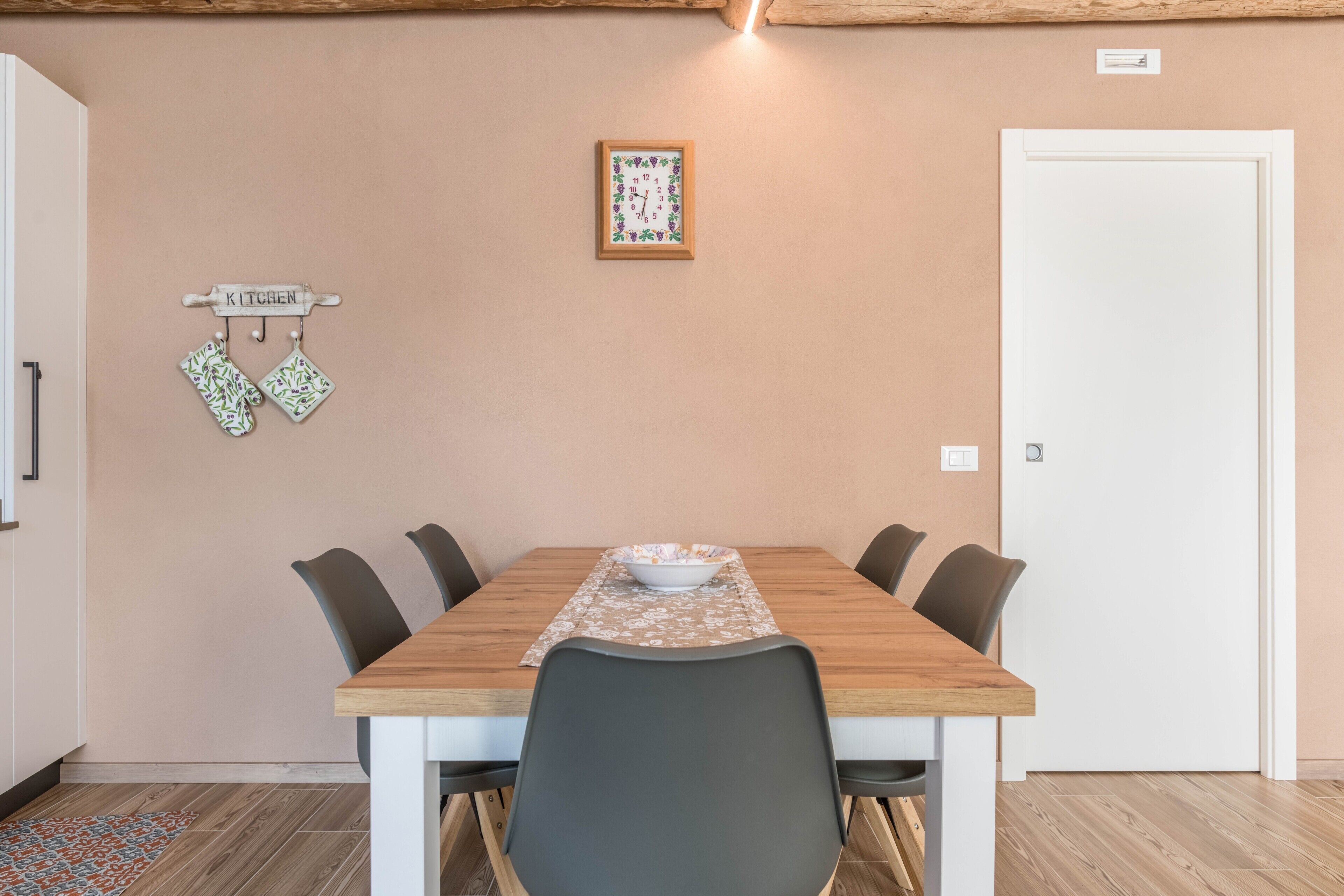 A dining area with a wooden table, chairs, a bowl, a kitchen sign, and a door.