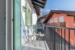 A balcony with a table and chairs, a green door, and a view of buildings and mountains.