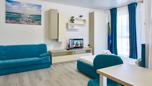 Uma sala de estar moderna com um sofá azul, uma TV em um móvel, uma mesinha e uma janela com cortinas.