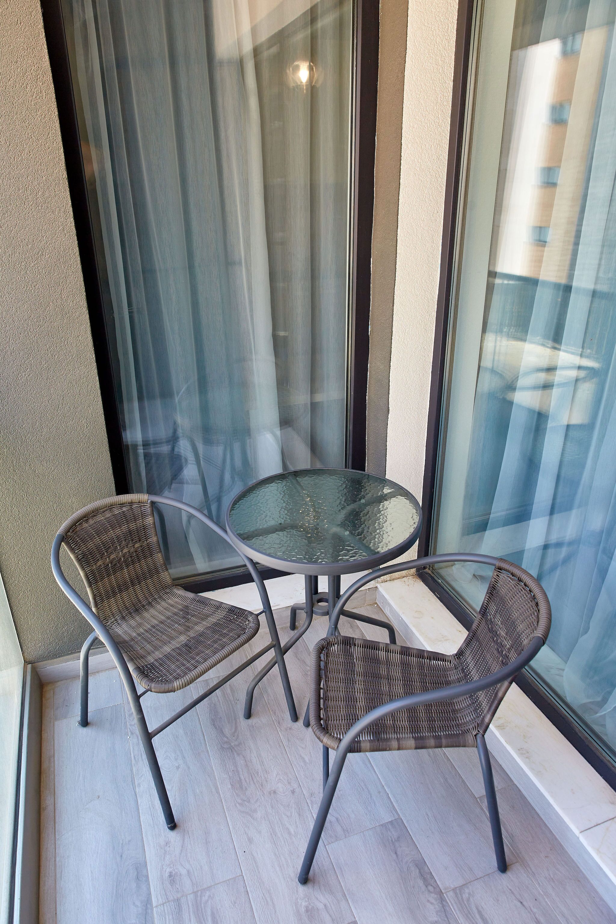 A small balcony with two wicker chairs and a glass table.