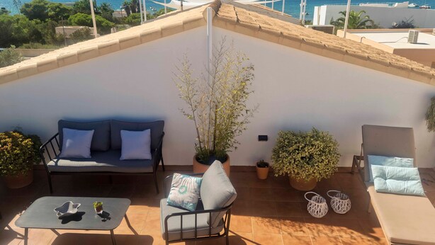 Eine Dachterrasse mit einer Couch, einem kleinen Tisch, Topfpflanzen und Meerblick.