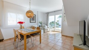 Ein modernes Wohnzimmer mit Essbereich, großen Fenstern und einem Fernseher.