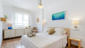 Ein Schlafzimmer mit einem großen Bett, einem Nachttisch, einer Kommode, einem Spiegel, einem Wandbild und einem Fenster.