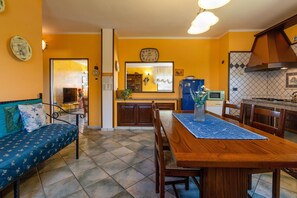 Un comedor con mesa y sillas de madera, alfombra azul y un sofá con cojines estampados.