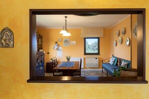 Una habitación con una mesa de comedor, sillas, un sofá, un radiador y una ventana que da a árboles.