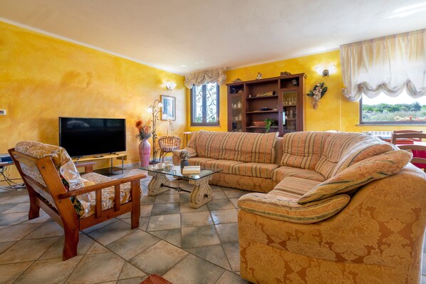 A living room with a sofa, a chair, a television, a bookshelf, and a window with curtains.