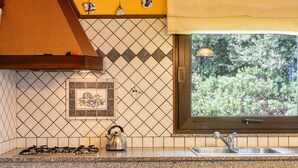Una cocina con estufa a gas, tetera, lavamanos y ventana con vistas a zonas verdes.