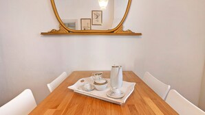 Uma mesa de jantar com um conjunto de chá branco em bandeja e um jarro, rodeada por cadeiras brancas, com um espelho grande em cima.