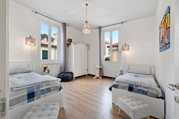 A bedroom with two beds, a chandelier, a wardrobe, and a small table.