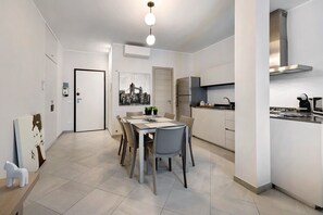 A modern kitchen with a stainless steel range hood, a dining area with a table and chairs, and a hallway with a door and artwork.
