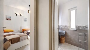 A bedroom with a bed, bedside tables, and a nightstand. There is a bathroom with a sink, mirror, and towel rack. - Vacation Apartment '4 Passi Mare 2' with Balconies, A/C and Wi-Fi (Finale Ligure)