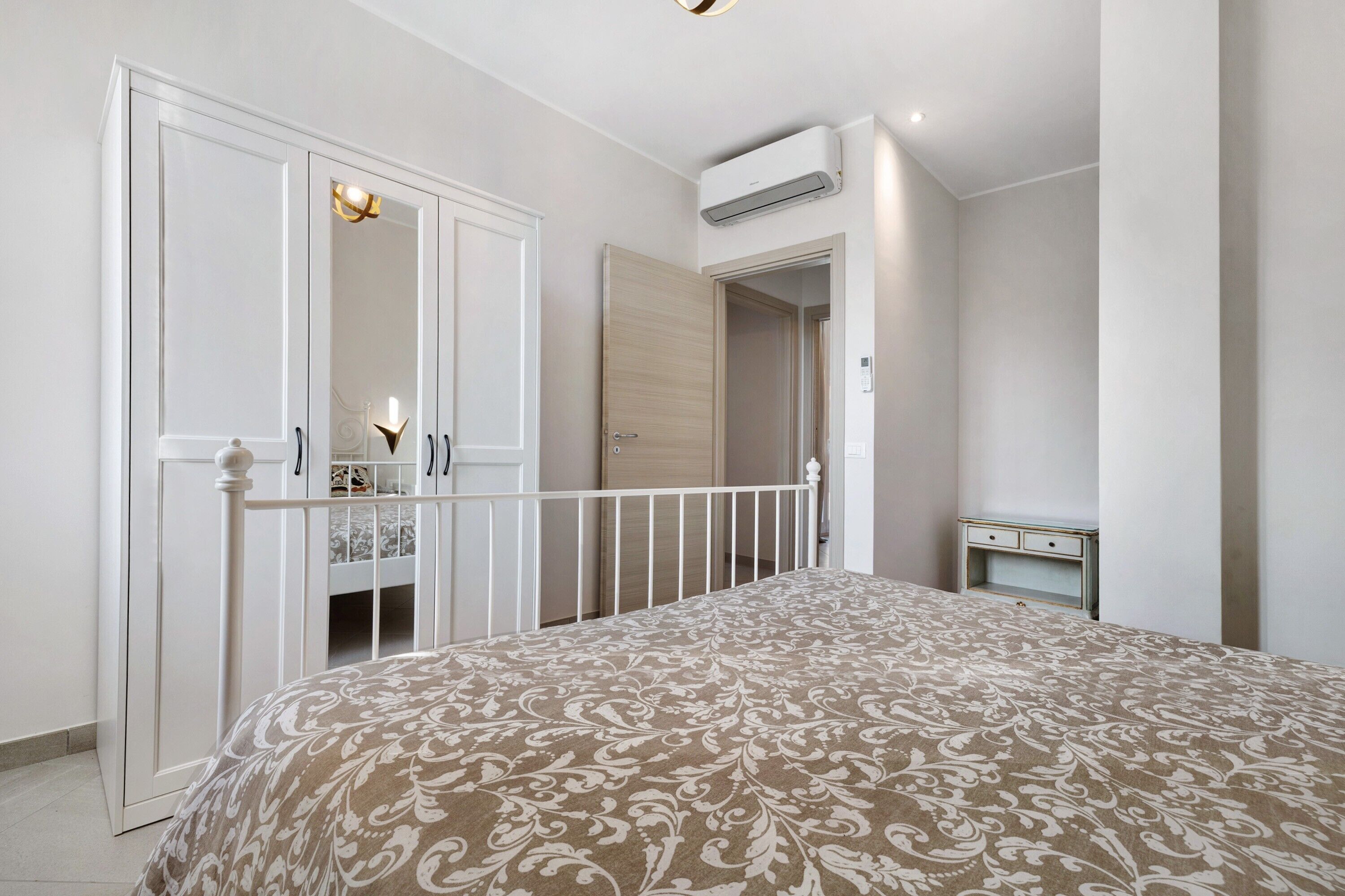 A bedroom with a bed, a wardrobe, a bedside table, and an air conditioning unit.