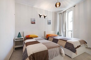 A bedroom with two beds, a nightstand, a small Christmas tree, and a window with curtains.