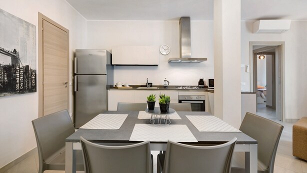 A modern kitchen with a stainless steel refrigerator, a gas stove, and a microwave. There is a dining table with four chairs and two potted plants on it. - Vacation Apartment '4 Passi Mare 2' with Balconies, A/C and Wi-Fi (Finale Ligure)