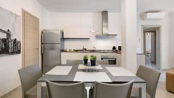 A modern kitchen with a stainless steel refrigerator, a gas stove, and a microwave. There is a dining table with four chairs and two potted plants on it.