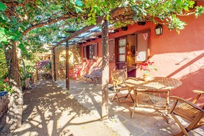 Un espace extérieur abrité, aménagé avec une table et des chaises, une pergola et un bâtiment dont le mur est rouge et dont la porte est visible.