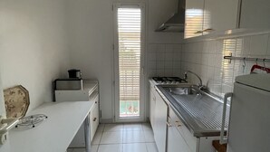 Keittiössä on valkoiset kaapit, ruostumattomasta teräksestä valmistettu työtaso ja laatoitettu lattia.