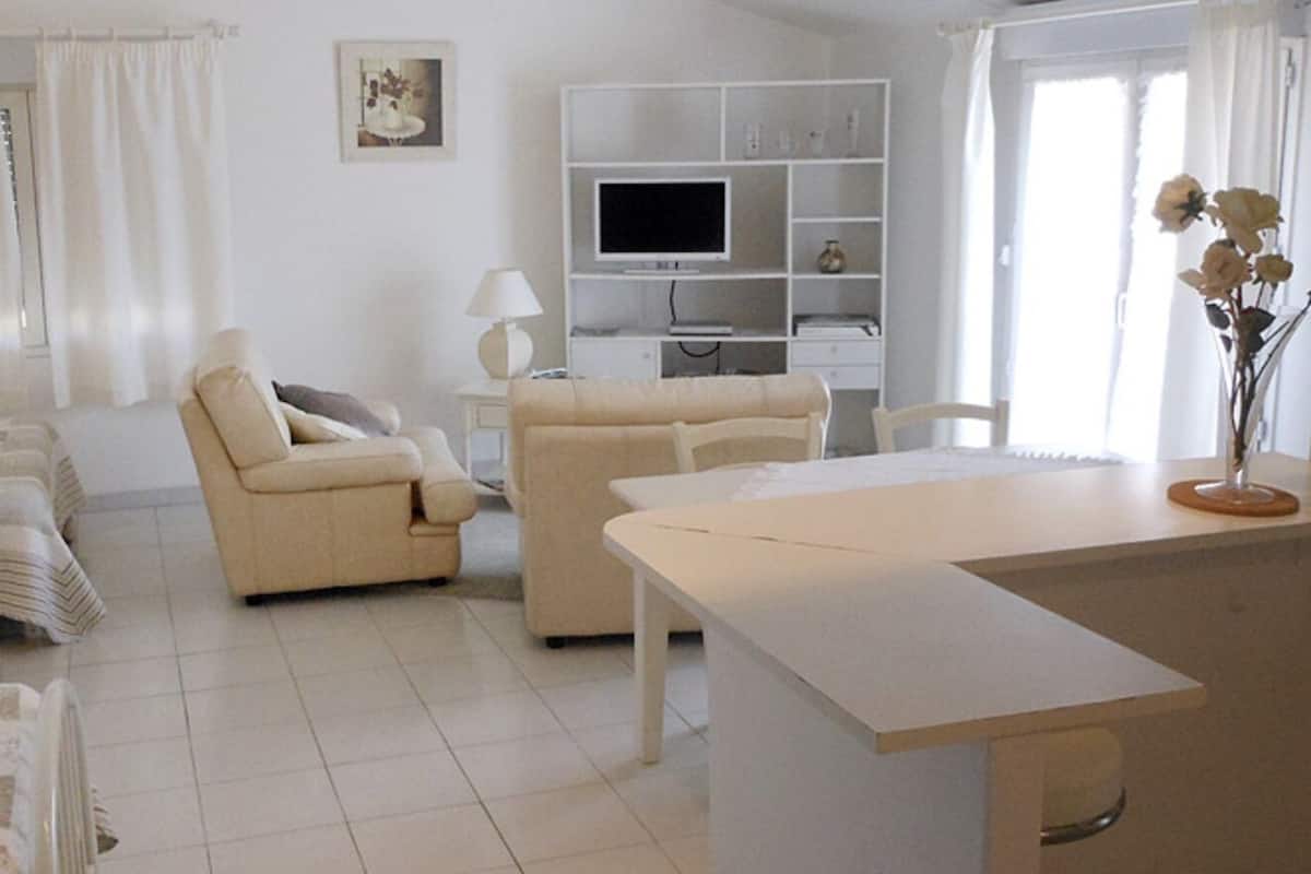 A modern, well-lit living room with a sofa, armchair, and a TV on a white entertainment unit.