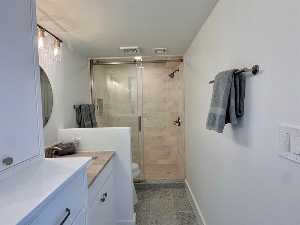 A modern bathroom with a glass shower enclosure, a white vanity with drawers, and a towel rack on the wall.