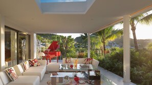 Un salon moderne avec une table basse en verre, des canapés blancs et un piano rouge.