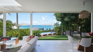 Un salon moderne offrant une vue sur l’océan, une piscine et une végétation luxuriante.
