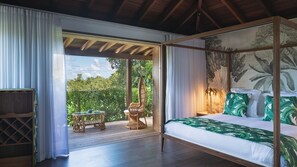 Une chambre spacieuse dotée d’un lit à baldaquin, offrant une vue sur une végétation luxuriante et comprenant une terrasse en bois avec des meubles d’extérieur.
