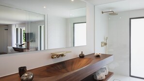 Une salle de bain moderne avec un meuble-lavabo en bois, un grand miroir, une douche équipée d’un pommeau de douche à main et un porte-serviettes.