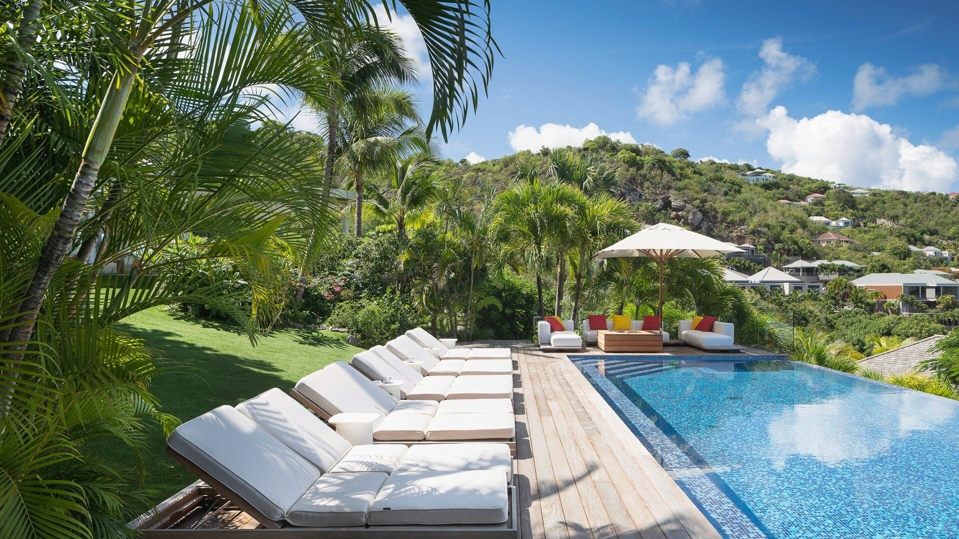 Zona junto a la piscina con sillones de descanso, una piscina y vistas a una colina con casas.