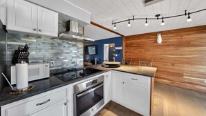 A modern kitchen with white cabinets, a black countertop, and a wooden wall. - The Lake Home - Beautiful Oasis In The Heart Of Florida! 2 Bedroom Home by RedAwning (Haines City)