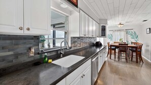 A kitchen with white cabinets, a black countertop, and a dining area with wooden chairs and a table. - The Lake Home - Beautiful Oasis In The Heart Of Florida! 2 Bedroom Home by RedAwning (Haines City)