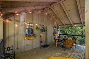A covered wooden deck with a table and chairs, surrounded by wooden walls and string lights. - Cliff Haven 1 Bedroom Cabin by RedAwning (Townsend)