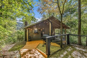A wooden cabin with a deck and a fenced area, surrounded by trees.