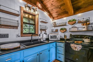 A kitchen with blue cabinets, a black stove, and wooden beams on the ceiling. - Cliff Haven 1 Bedroom Cabin by RedAwning (Townsend)