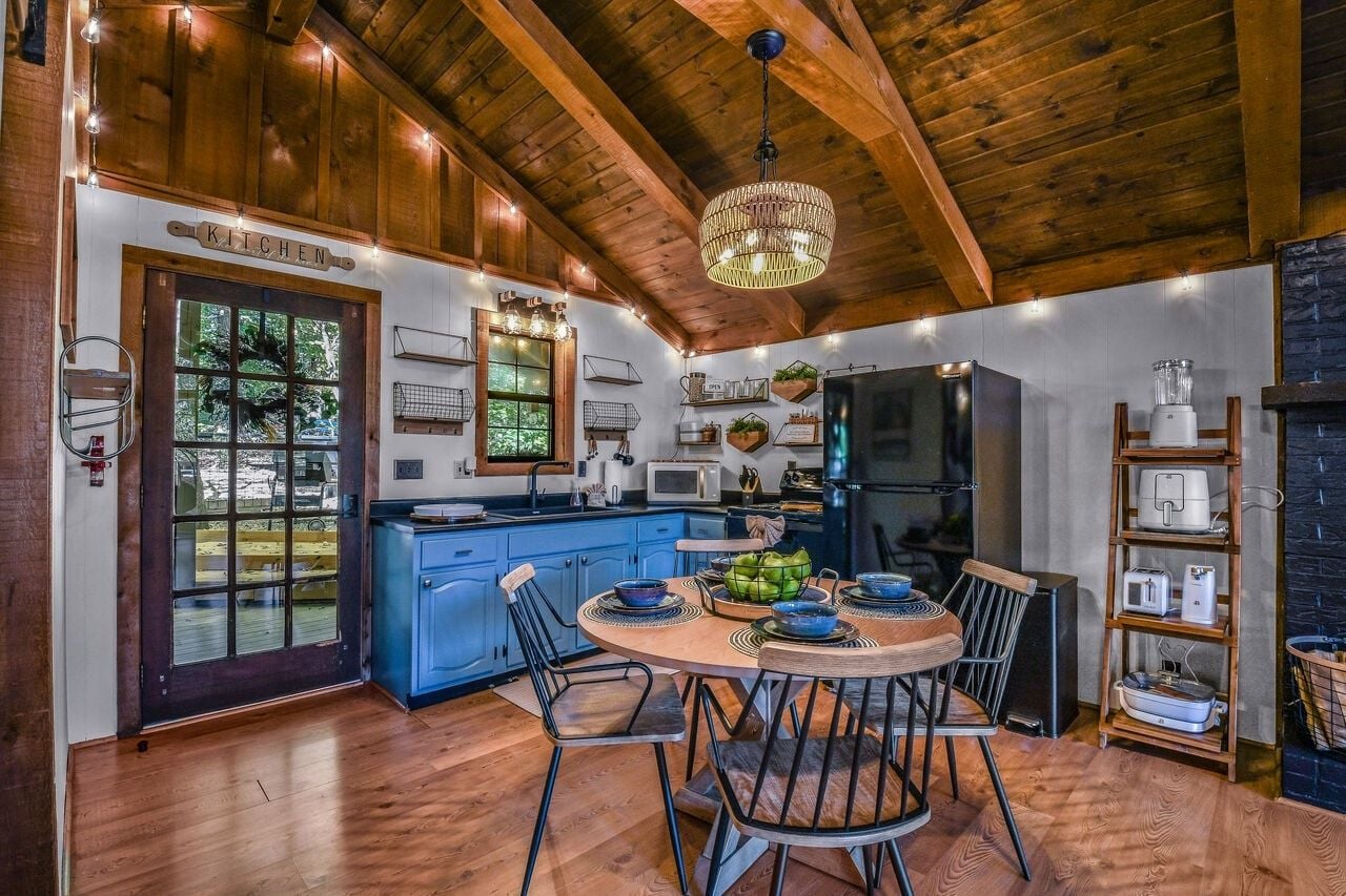 A kitchen with wooden ceiling beams, a dining table with chairs, and a refrigerator.