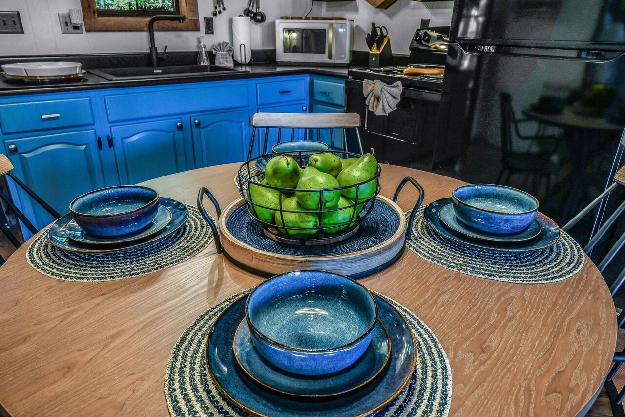 A kitchen with blue cabinets, a round wooden table with blue bowls, and a fruit basket.