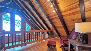A wooden interior with a sloped ceiling, a wooden deck, a red bench, and a table with a lamp. - High Mountain Cabin Long Range Mountain Views at 4,000 Ft above Sea Level (Bryson City)