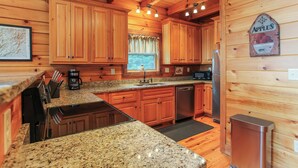 A wooden cabin kitchen with granite countertops, wooden cabinets, a stainless steel refrigerator, and a coffee maker. - High Mountain Cabin Long Range Mountain Views at 4,000 Ft above Sea Level (Bryson City)