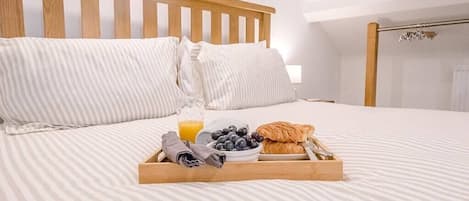 A neatly made bed with a tray of breakfast items including croissants, a bowl of blueberries, and a glass of orange juice.