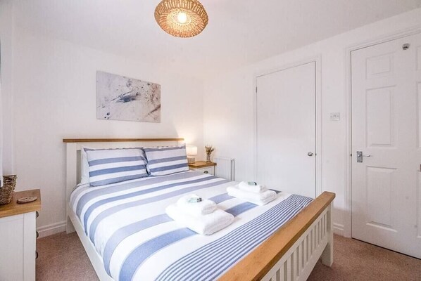 Ein Schlafzimmer mit einem Bett, einem Nachttisch, einer Lampe, einem Wandbild und einer Tür.